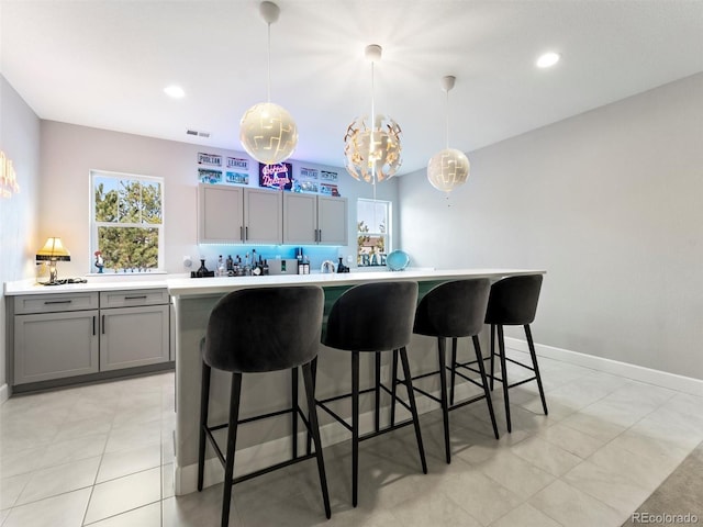 kitchen featuring visible vents, gray cabinets, a breakfast bar area, light countertops, and baseboards