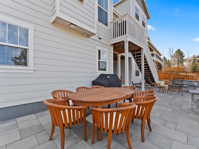 view of patio with a grill, outdoor dining space, stairs, and fence