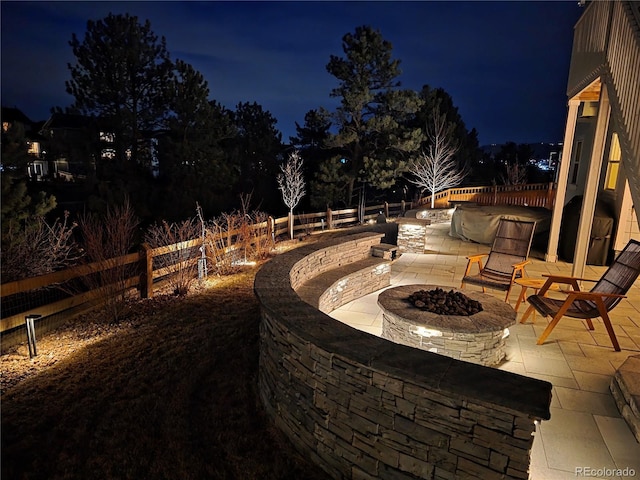 patio at night featuring a fire pit and fence