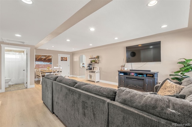 living area featuring arched walkways, light wood finished floors, recessed lighting, a glass covered fireplace, and baseboards