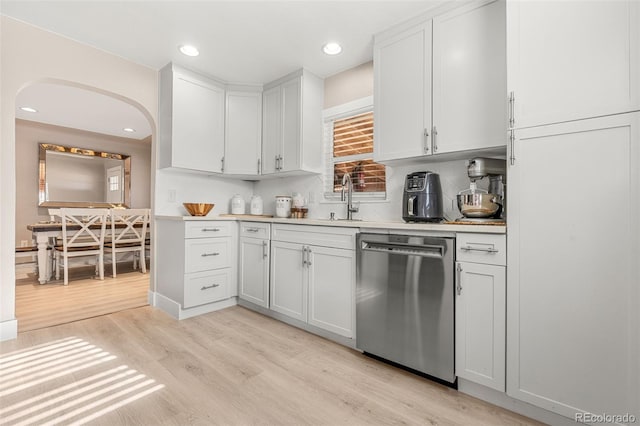 kitchen with arched walkways, light countertops, light wood-style flooring, white cabinetry, and dishwasher