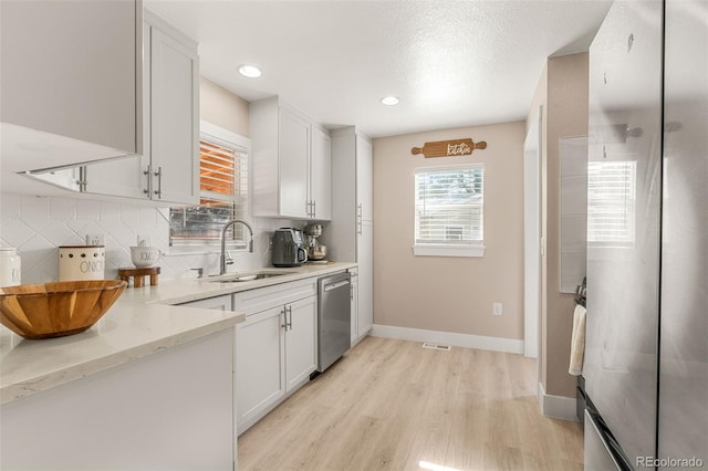 kitchen featuring tasteful backsplash, light wood-style flooring, stainless steel dishwasher, white cabinetry, and a sink