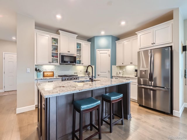 kitchen with a sink, light wood finished floors, appliances with stainless steel finishes, and white cabinetry