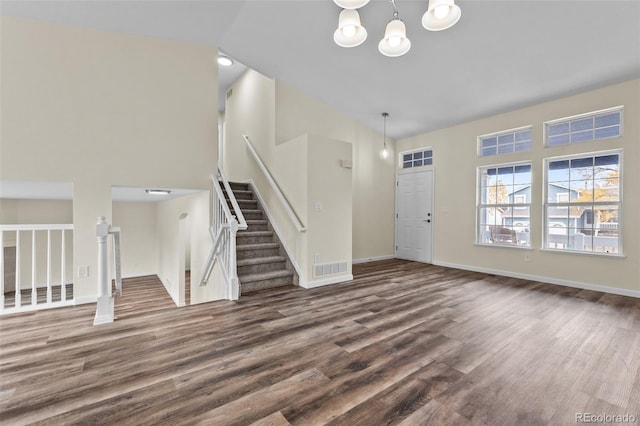 unfurnished living room with dark wood-type flooring, high vaulted ceiling, and a notable chandelier