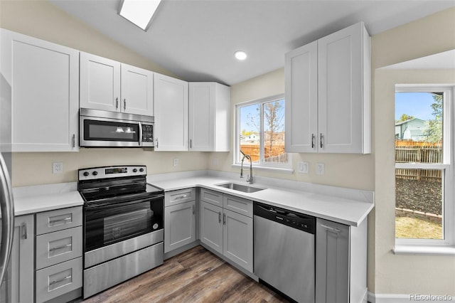 kitchen with vaulted ceiling, dark hardwood / wood-style floors, sink, gray cabinets, and stainless steel appliances