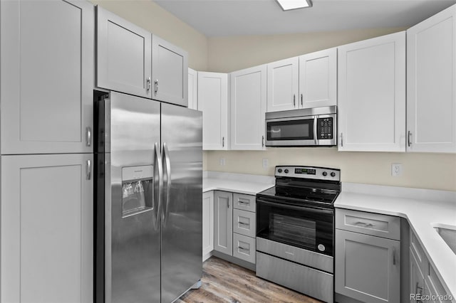 kitchen featuring vaulted ceiling, stainless steel appliances, white cabinetry, and light hardwood / wood-style floors