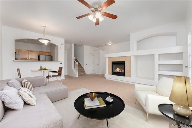5255 Memphis St Unit 219, Denver, CO 80239 - living room featuring stairs, a ceiling fan, light colored carpet, a tiled fireplace, and built in shelves