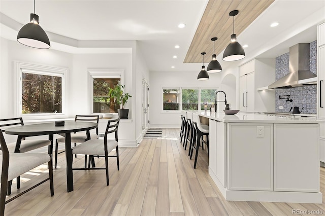 kitchen featuring hanging light fixtures, decorative backsplash, white cabinets, and wall chimney exhaust hood