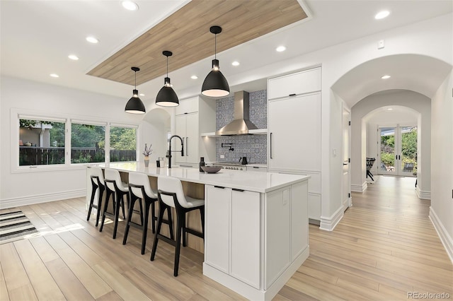 kitchen featuring decorative light fixtures, sink, white cabinets, a center island with sink, and wall chimney exhaust hood