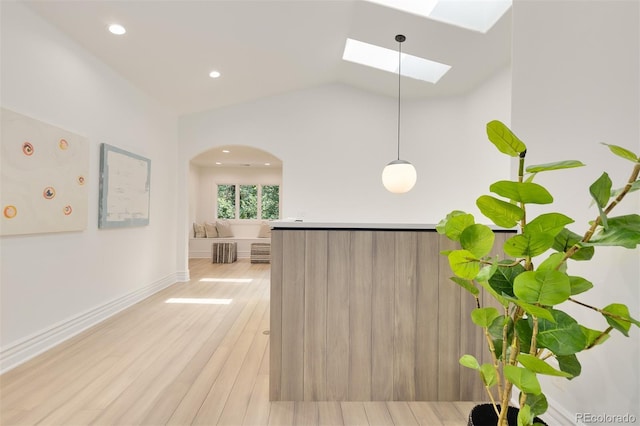 kitchen with hanging light fixtures, light hardwood / wood-style floors, and vaulted ceiling with skylight