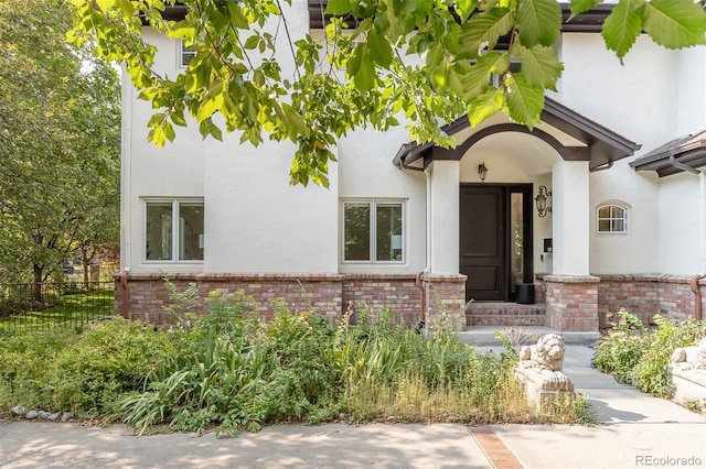 doorway to property featuring stucco siding, fence, and brick siding