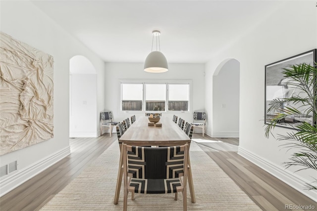 dining space featuring baseboards, arched walkways, and light wood finished floors