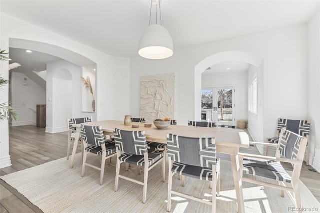 dining area with arched walkways, light wood finished floors, and baseboards