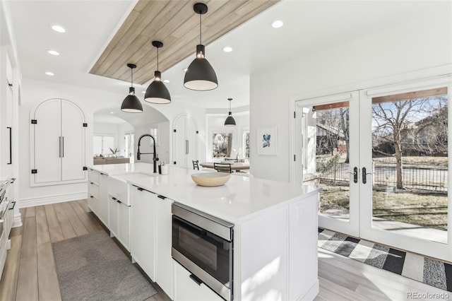 kitchen with stainless steel microwave, light countertops, french doors, white cabinets, and a sink