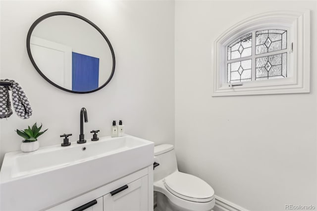 half bathroom with toilet, vanity, and baseboards