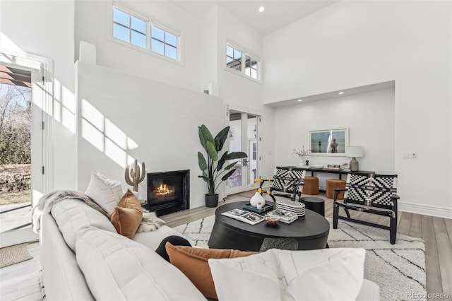 living room with baseboards, recessed lighting, a towering ceiling, wood finished floors, and a glass covered fireplace