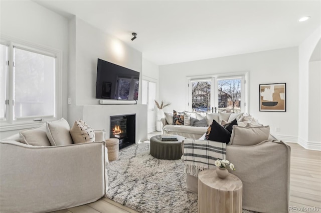 living area featuring a glass covered fireplace, recessed lighting, baseboards, and wood finished floors