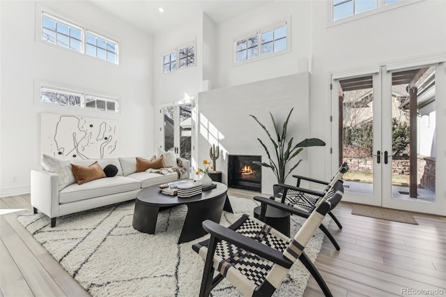 living area with a glass covered fireplace, french doors, a towering ceiling, and wood finished floors