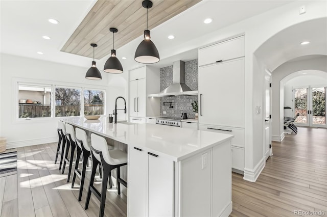 kitchen featuring light wood-style flooring, a sink, white cabinetry, wall chimney range hood, and decorative backsplash