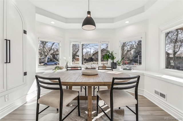 dining room featuring a raised ceiling, visible vents, a wealth of natural light, and light wood-type flooring