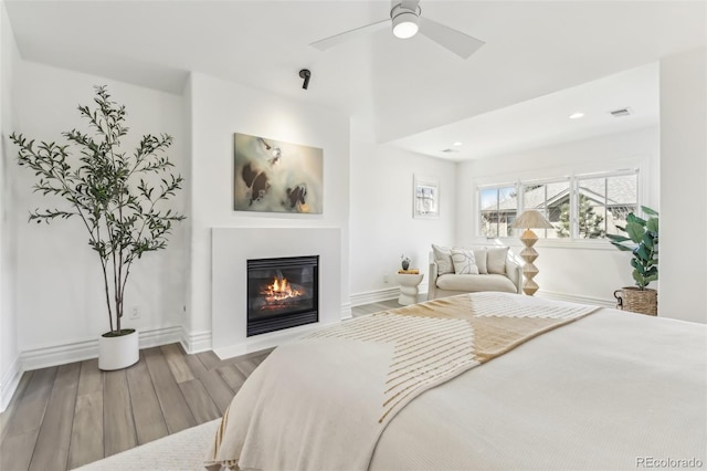 bedroom with visible vents, a ceiling fan, a glass covered fireplace, wood finished floors, and baseboards