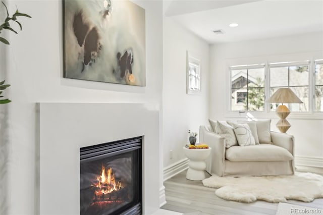 living area featuring visible vents, baseboards, recessed lighting, wood finished floors, and a glass covered fireplace