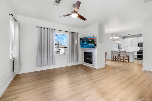 unfurnished living room with visible vents, baseboards, light wood-type flooring, ceiling fan with notable chandelier, and a fireplace