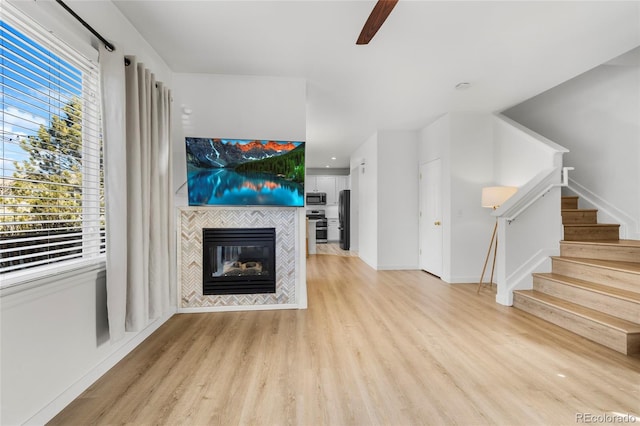 unfurnished living room with stairway, baseboards, light wood-type flooring, and a tile fireplace