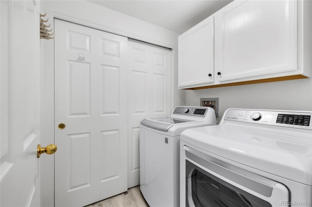 clothes washing area featuring light wood-style flooring, cabinet space, and washing machine and dryer