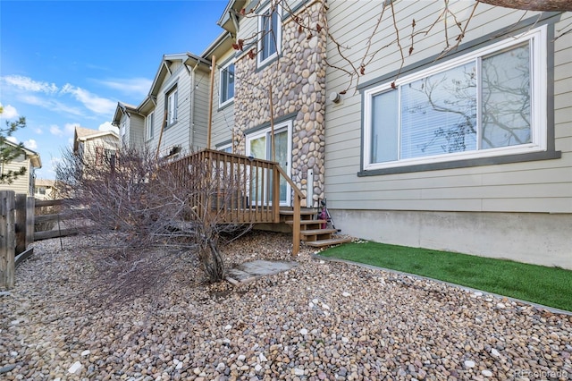 view of side of home featuring stone siding, a deck, and fence