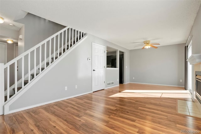 unfurnished living room featuring a tiled fireplace, ceiling fan, and light hardwood / wood-style flooring