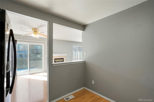 spare room with a tile fireplace, a healthy amount of sunlight, hardwood / wood-style floors, and ceiling fan