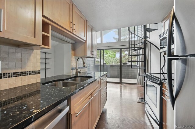 9797 E Peakview Ave Unit C10, Englewood, CO 80111 - kitchen featuring appliances with stainless steel finishes, a sink, decorative backsplash, dark stone countertops, and wood finished floors
