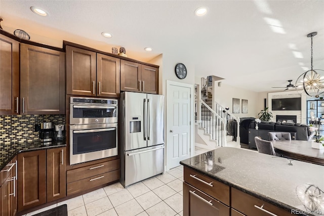 12693 W 82nd Ln, Arvada, CO 80005 - kitchen featuring stainless steel appliances, light tile patterned floors, a glass covered fireplace, a ceiling fan, and backsplash