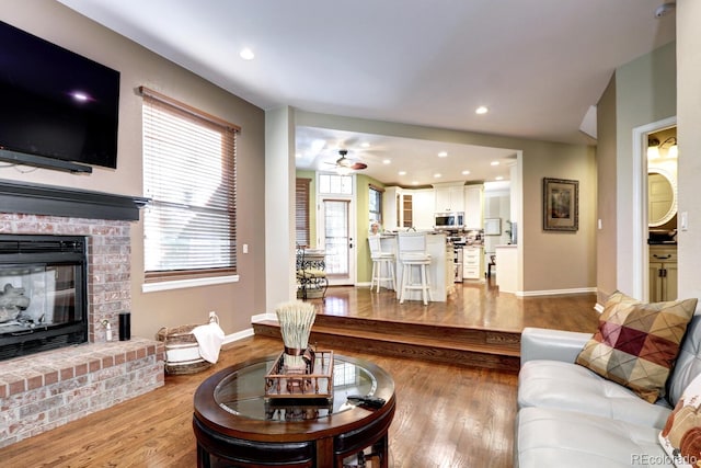 living room featuring ceiling fan, light hardwood / wood-style floors, and a brick fireplace