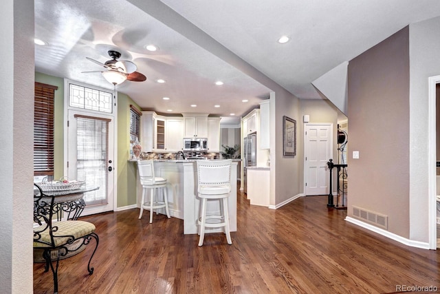 kitchen featuring a breakfast bar, appliances with stainless steel finishes, white cabinetry, dark hardwood / wood-style flooring, and kitchen peninsula