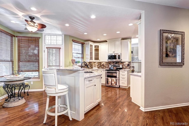 kitchen featuring a breakfast bar area, tasteful backsplash, appliances with stainless steel finishes, light stone countertops, and white cabinets