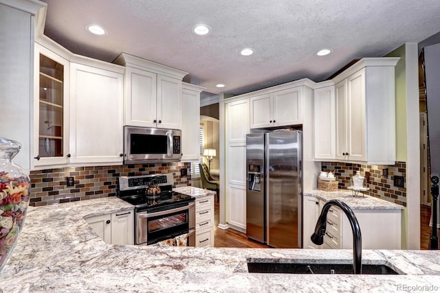 kitchen featuring appliances with stainless steel finishes, tasteful backsplash, white cabinetry, sink, and light stone countertops