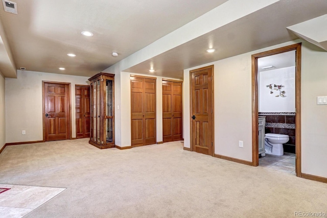 unfurnished bedroom with connected bathroom, light carpet, and two closets