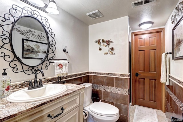 bathroom featuring tile walls, vanity, a textured ceiling, and toilet