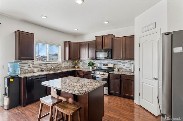 kitchen featuring dark brown cabinets, a sink, wood finished floors, backsplash, and black appliances