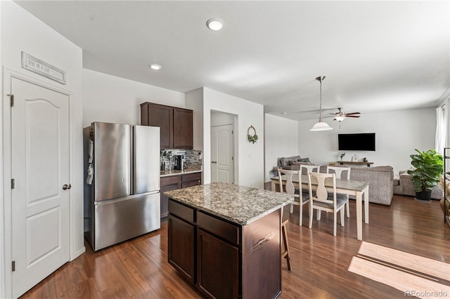 kitchen with freestanding refrigerator, dark brown cabinetry, open floor plan, ceiling fan, and a center island