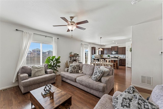 living room with baseboards, ceiling fan, dark wood finished floors, and visible vents