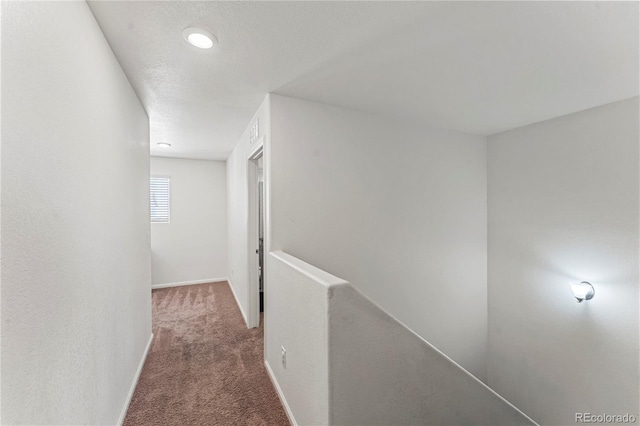 hallway featuring baseboards, carpet flooring, a textured ceiling, and an upstairs landing