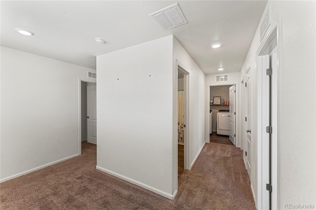 hall with carpet floors, baseboards, visible vents, and washing machine and dryer