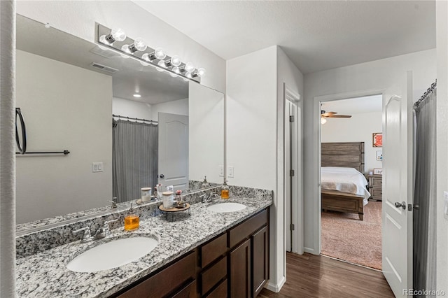 ensuite bathroom with a sink, ceiling fan, wood finished floors, and visible vents