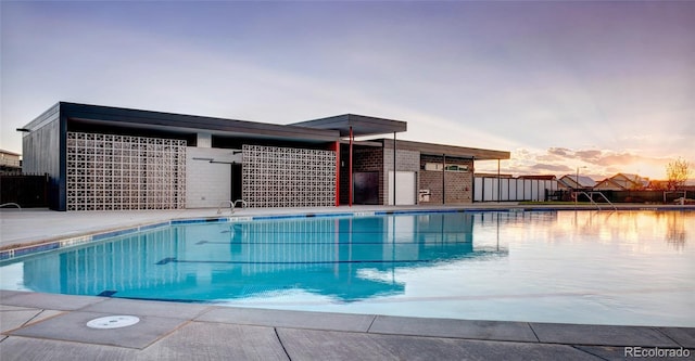 pool at dusk featuring fence and a community pool