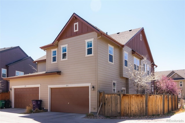 exterior space with concrete driveway, board and batten siding, an attached garage, and fence