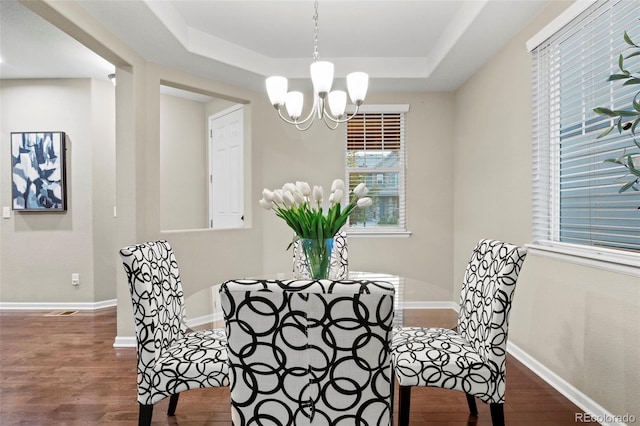 dining area featuring a chandelier, a raised ceiling, and dark wood-type flooring