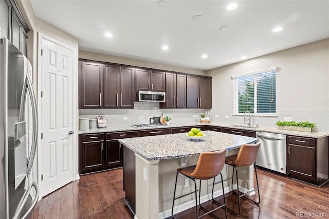 kitchen with appliances with stainless steel finishes, light stone counters, a kitchen island, dark hardwood / wood-style flooring, and sink